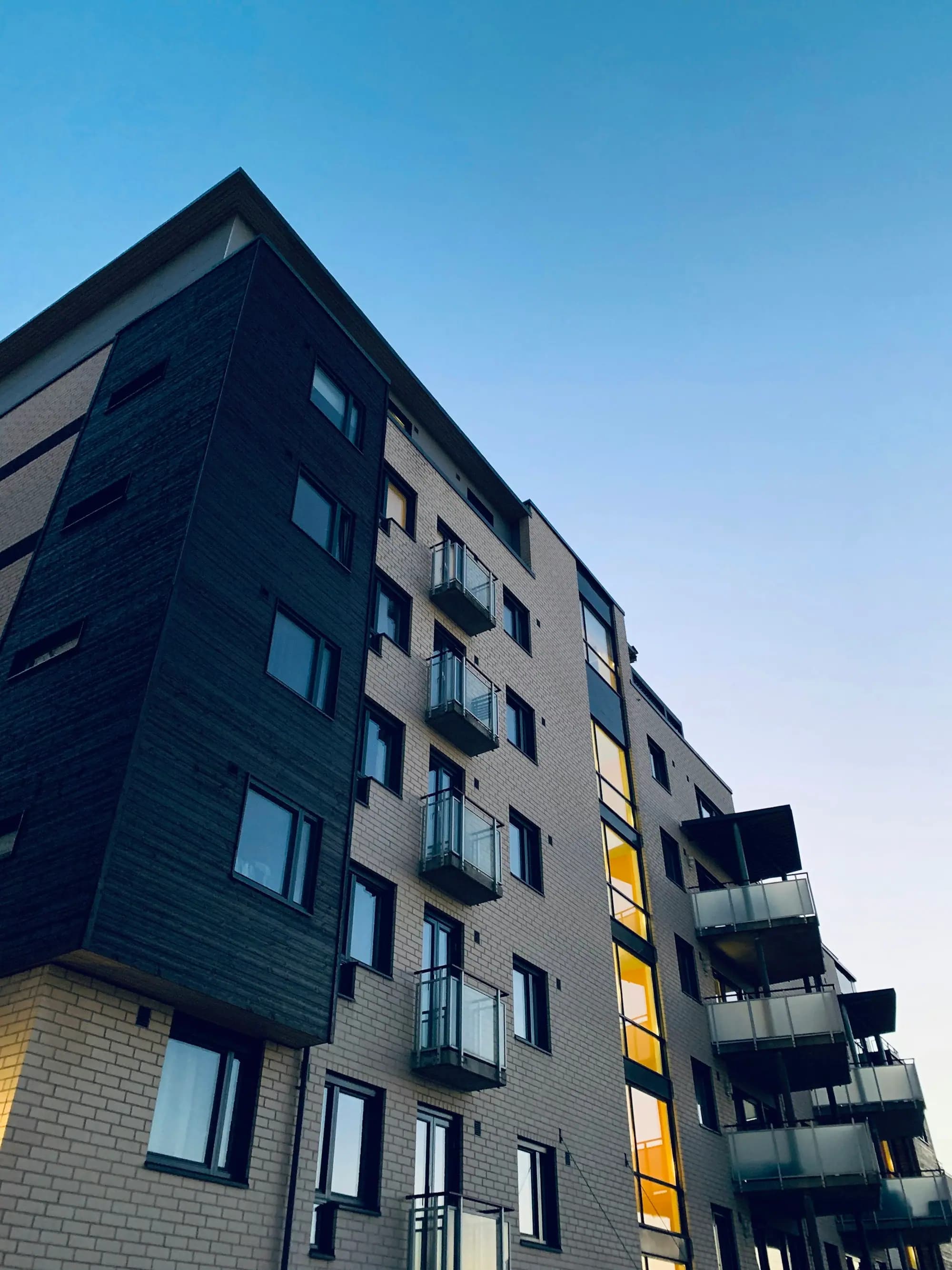 Fachada de un edificio residencial con balcones al caer la tarde, con las luces encendidas